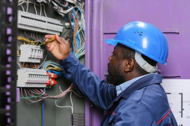 Afro-Amerikalı elektrikçi dağıtım panosunda elektrik tesisatı yapıyor.