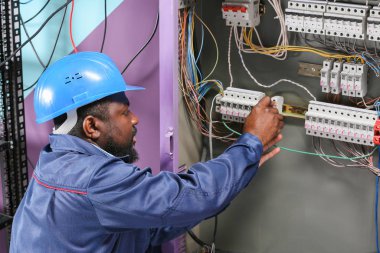 Afro-Amerikalı elektrikçi dağıtım panosunda elektrik tesisatı yapıyor.
