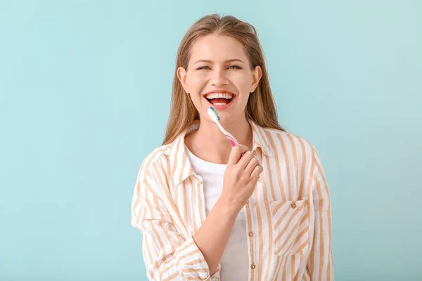 Young woman brushing teeth on color background — Stock Photo, Image