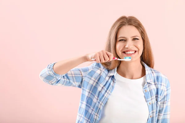 Young woman brushing teeth on color background — Stock Photo, Image