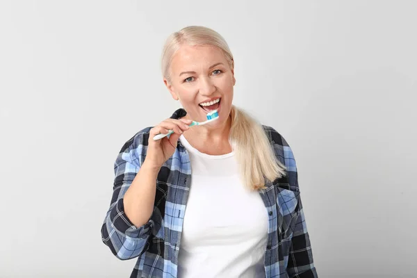 Starší žena čištění zubů na světlém pozadí — Stock fotografie