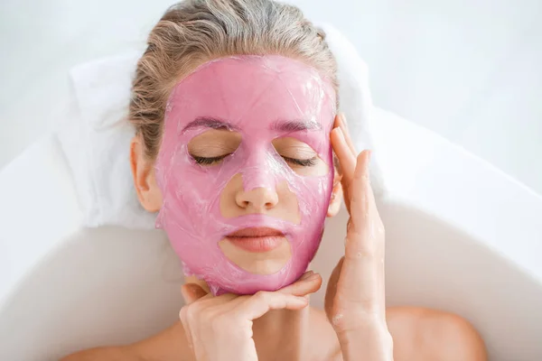 Hermosa mujer joven con máscara facial relajante en el baño —  Fotos de Stock