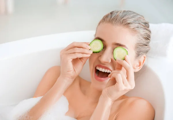 Hermosa mujer joven con rodajas de pepino tumbado en el baño —  Fotos de Stock