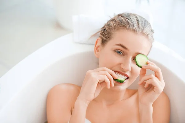 Hermosa mujer joven con rodajas de pepino tumbado en el baño —  Fotos de Stock