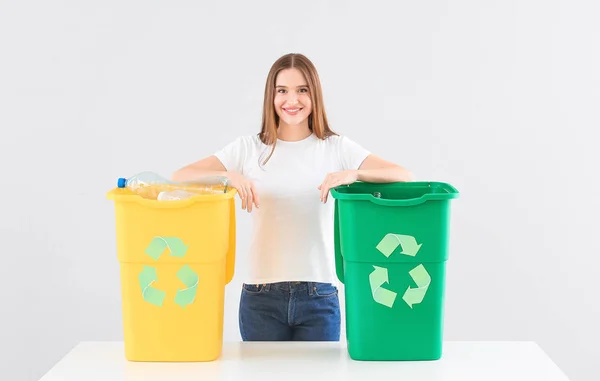 Mujer con contenedores de basura sobre fondo claro. Concepto de reciclaje —  Fotos de Stock