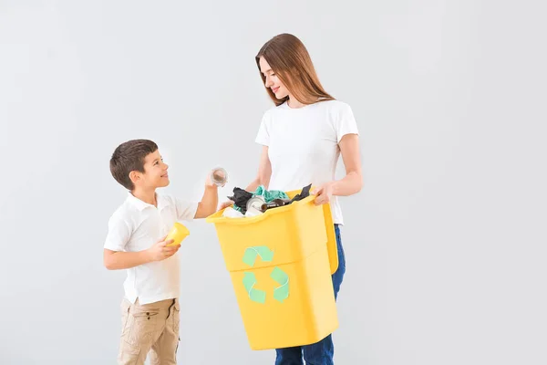 Moeder en zoon met container voor vuilnis op lichte achtergrond. Concept van recycling — Stockfoto