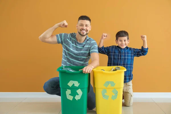 Feliz padre e hijo con recipientes para basura sobre fondo de color. Concepto de reciclaje — Foto de Stock