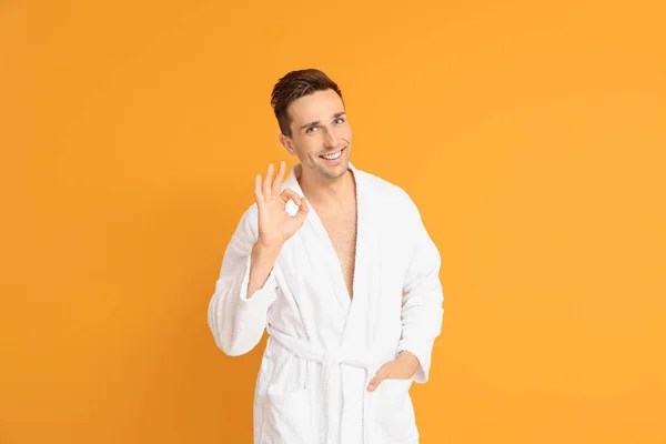 Handsome man in bathrobe showing OK gesture on color background — ストック写真