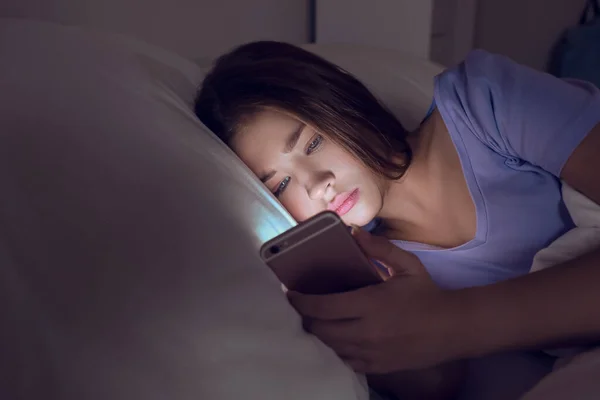Dospívající dívka s mobilním telefonem ležící v posteli v noci — Stock fotografie