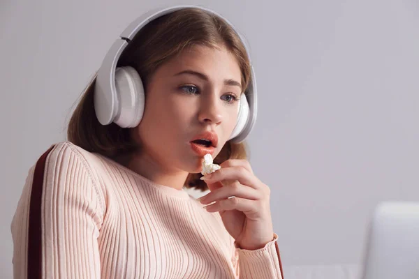 Adolescente con portátil comiendo palomitas de maíz mientras ve la película tarde en la noche —  Fotos de Stock