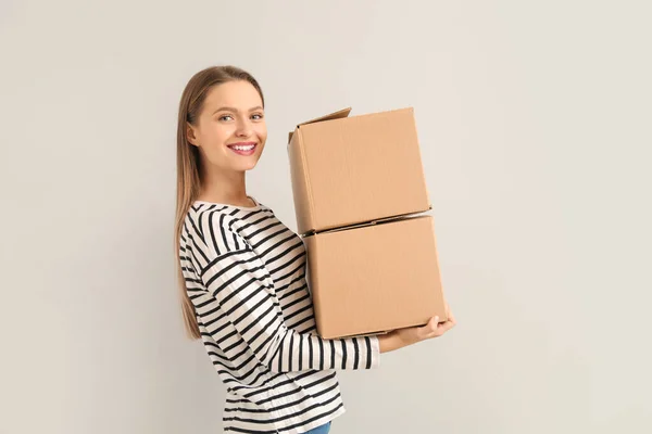 Happy young woman with moving boxes on light background — Stock Photo, Image