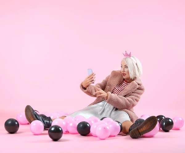 Удивлённая модная зрелая женщина с воздушными шарами и мобильным телефоном на цветном фоне — стоковое фото
