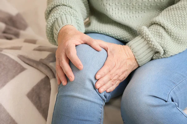 Senior woman suffering from pain in knee at home, closeup
