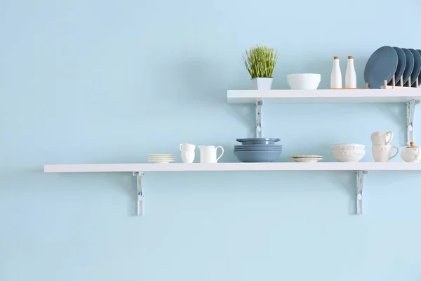 Shelves with tableware hanging on color wall — Stock Photo, Image