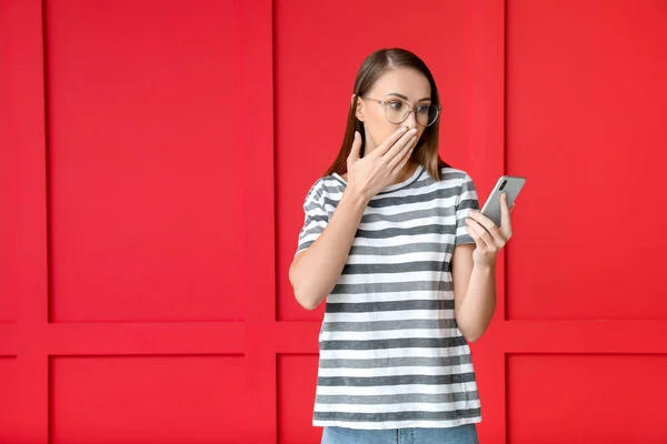 Worried young woman with mobile phone on color background — Stock Photo, Image