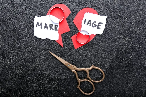 Broken heart, rings, scissors and torn paper with word MARRIAGE on dark background. Concept of divorce
