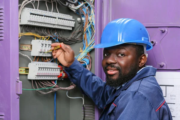 Eletricista afro-americano realizando fiação no quadro de distribuição — Fotografia de Stock