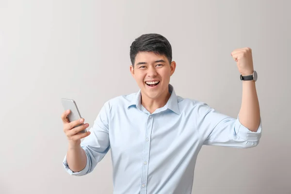 Jovem empresário asiático feliz com telefone celular no fundo claro — Fotografia de Stock