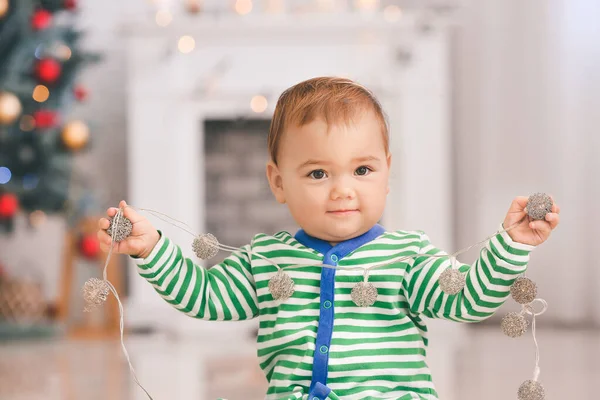 Cute little baby with garland in room decorated for Christmas — Stock Photo, Image