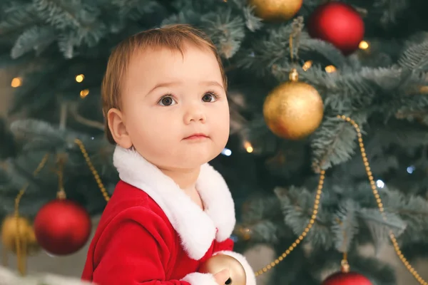 Cute little baby in Santa Claus costume near Christmas tree at home — Stock Photo, Image