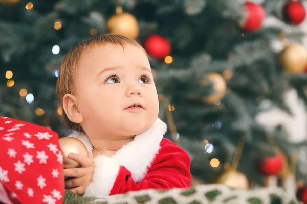 Bebê bonito em traje de Papai Noel perto da árvore de Natal em casa — Fotografia de Stock