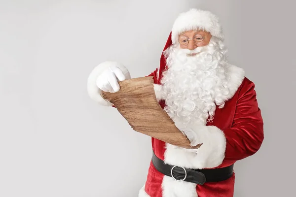 Weihnachtsmann liest Wunschliste auf hellem Hintergrund — Stockfoto