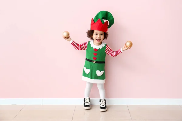 Little girl in costume of elf and with Christmas balls near color wall — Stock Photo, Image