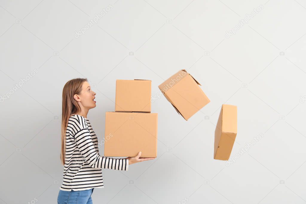Bothered woman dropping cardboard boxes on light background
