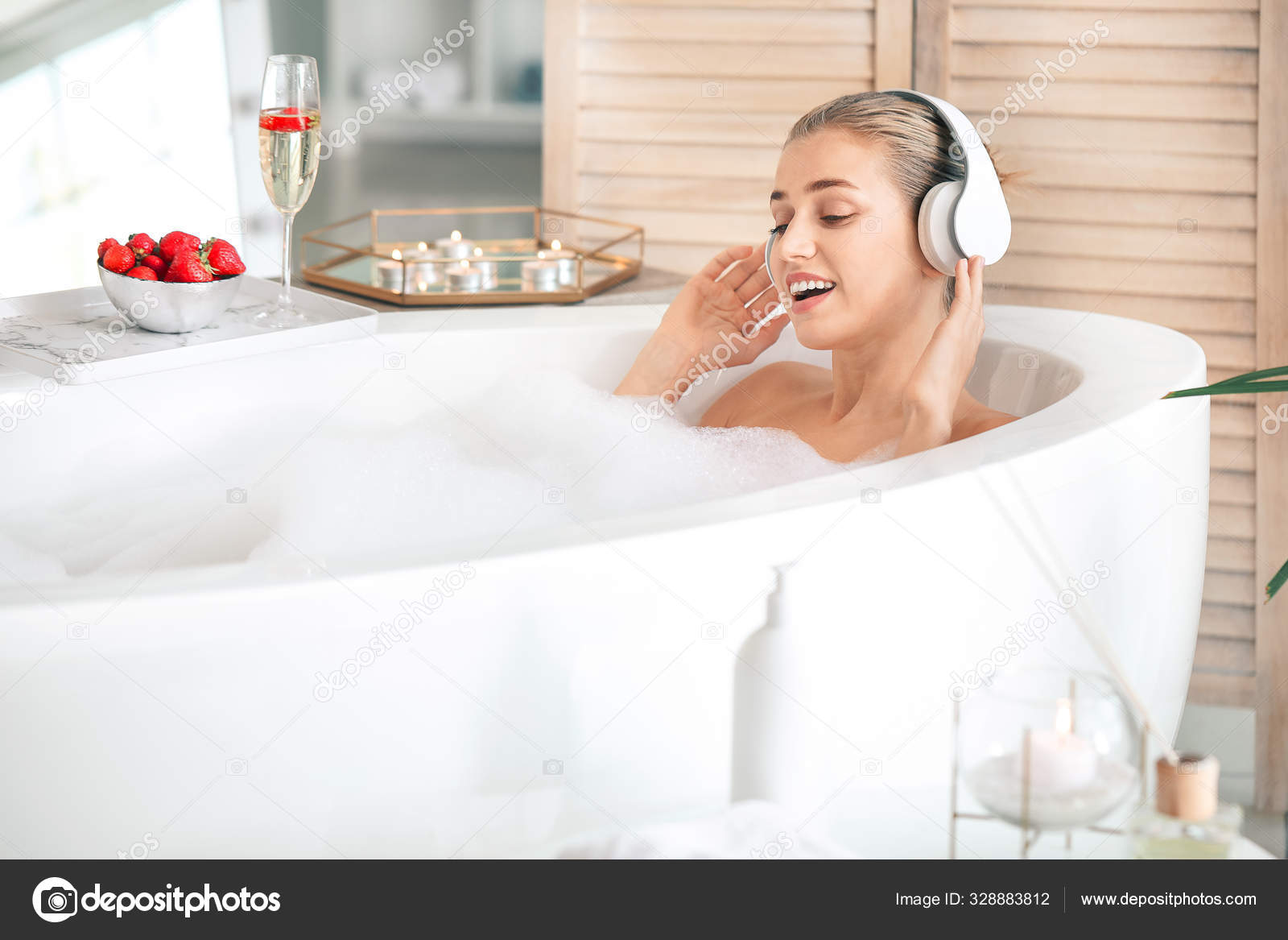 Beautiful young woman listening to music in bathroom Stock Photo by