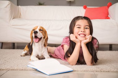 Evde sevimli bir av köpeği olan küçük Asyalı kız kitap okuyor.