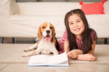 Evde sevimli bir av köpeği olan küçük Asyalı kız kitap okuyor.