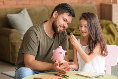 Evde domuz kumbarası olan baba ve küçük kızı.