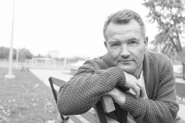 Sonbahar parkındaki olgun bir adamın siyah beyaz portresi.