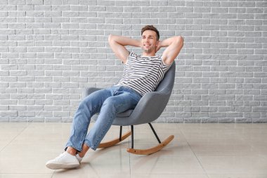 Yakışıklı adam tuğla duvarın yanında oturuyor.