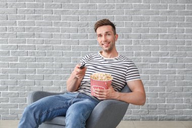 Yakışıklı adam gri duvarın yanında otururken film izliyor.