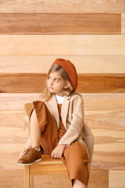 Sonbahar kıyafetleri içinde tahta duvarın yanında oturan tatlı küçük kız.