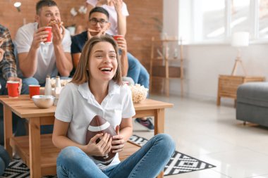 Arkadaşları olan genç bir kadın televizyonda ragbi seyrediyor.