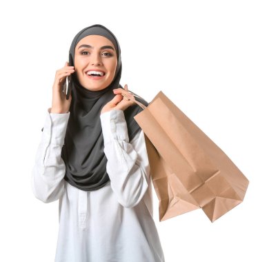 Alışveriş çantalı güzel bir Arap kadın beyaz arka planda cep telefonuyla konuşuyor.