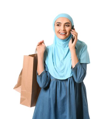 Alışveriş çantalı güzel bir Arap kadın beyaz arka planda cep telefonuyla konuşuyor.