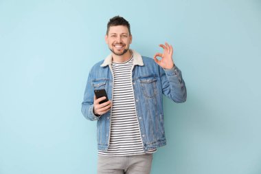 Cep telefonlu mutlu adam renk arkaplanında Tamam hareketi gösteriyor