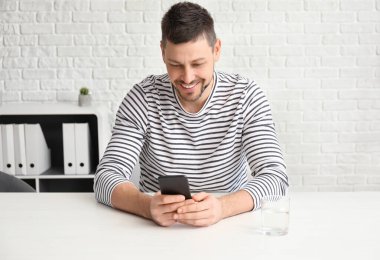 Cep telefonu olan adam masada oturuyor.