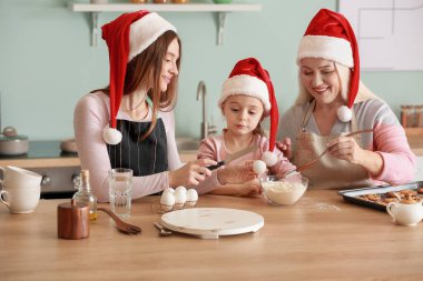 Küçük kızı ve annesiyle birlikte genç bir kadın evde Noel kurabiyesi pişiriyor.