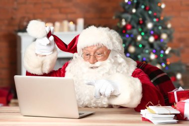 Noel Baba dizüstü bilgisayarıyla Noel için dekore edilmiş odasında postalarını kontrol ediyor.