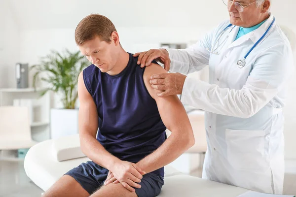 Зрілий лікар вивчає спортсмена з болем у суглобах у клініці — стокове фото