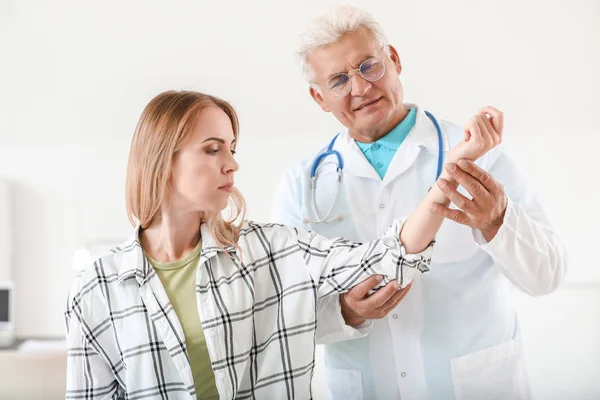 Rijpe arts onderzoeken jonge vrouw met gewrichtspijn in kliniek — Stockfoto