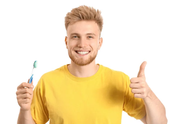 Mladý muž se zubním kartáčkem ukazující palec nahoru na bílém pozadí — Stock fotografie