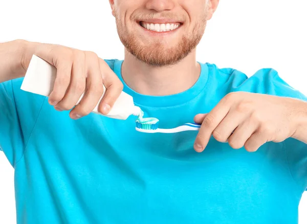 Mladý muž se zubním kartáčkem a pastou na bílém pozadí — Stock fotografie
