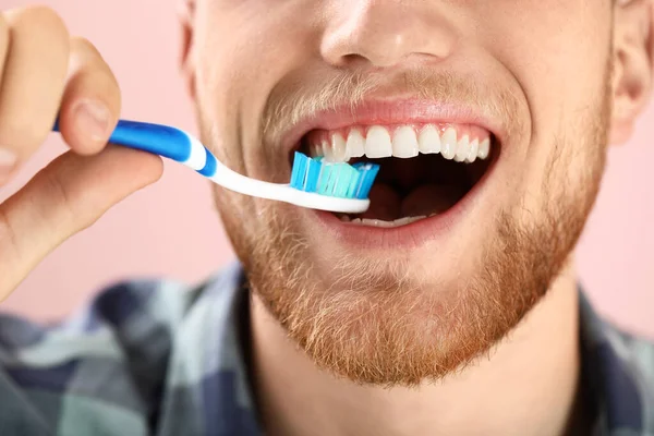 Young man brushing teeth on color background, closeup — Stock Photo, Image