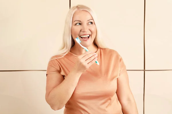 Mature woman brushing teeth on color background — Stock Photo, Image