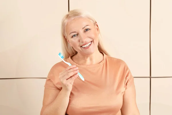 Reife Frau beim Zähneputzen auf farbigem Hintergrund — Stockfoto